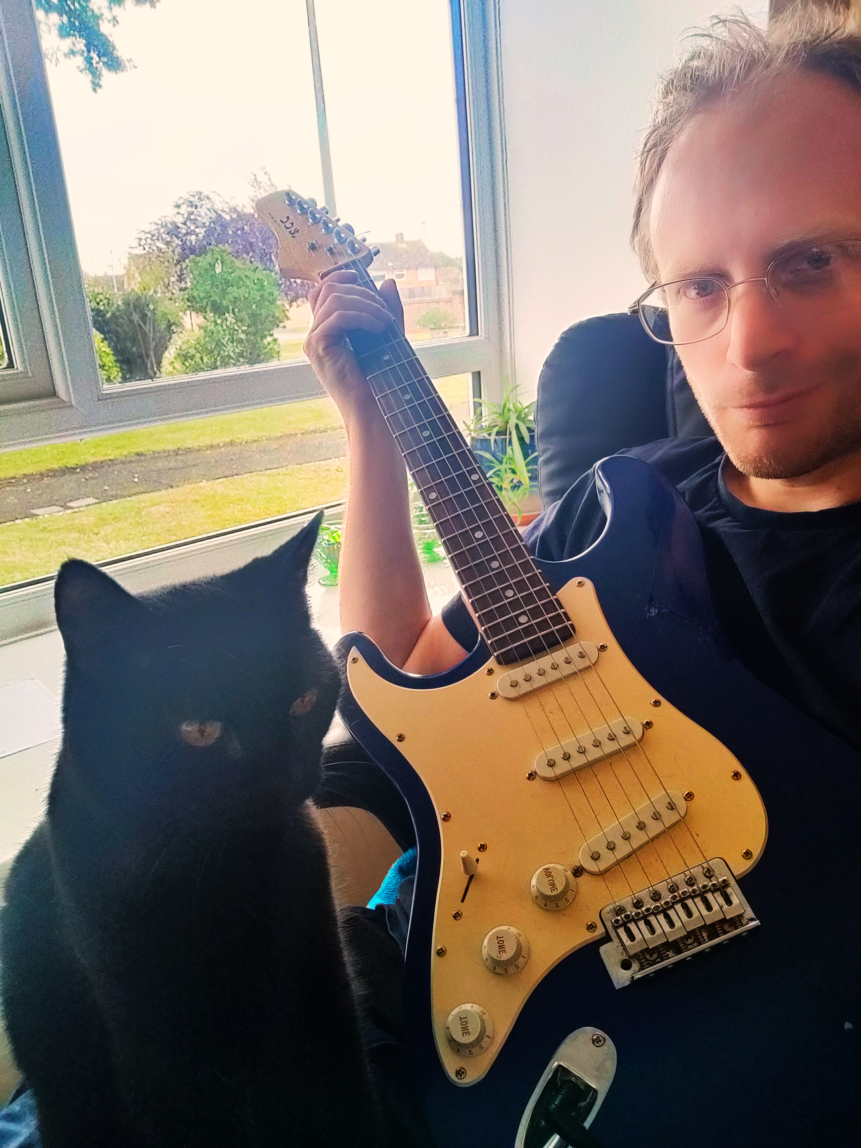 Kieran Simkin seated with an electric guitar and black cat