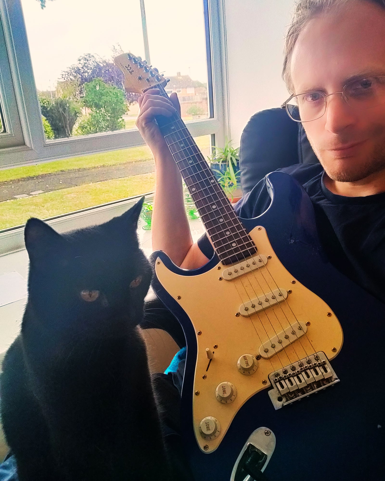 Kieran Simkin seated with an electric guitar beside a black cat